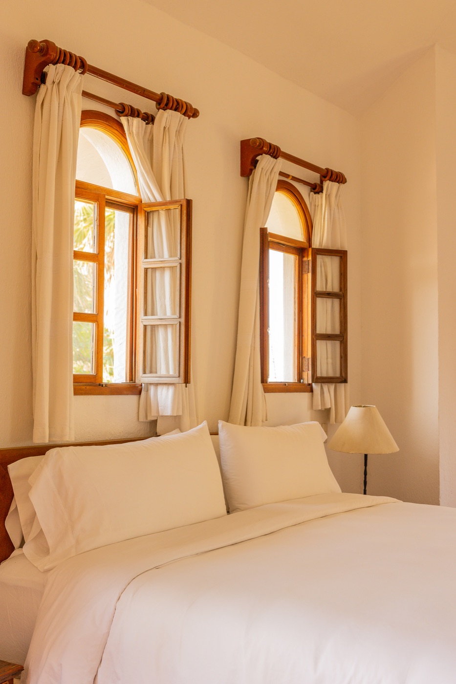 Habitación del Hotel Santa Fe con cama y ventanas arqueadas de madera con cortinas blancas